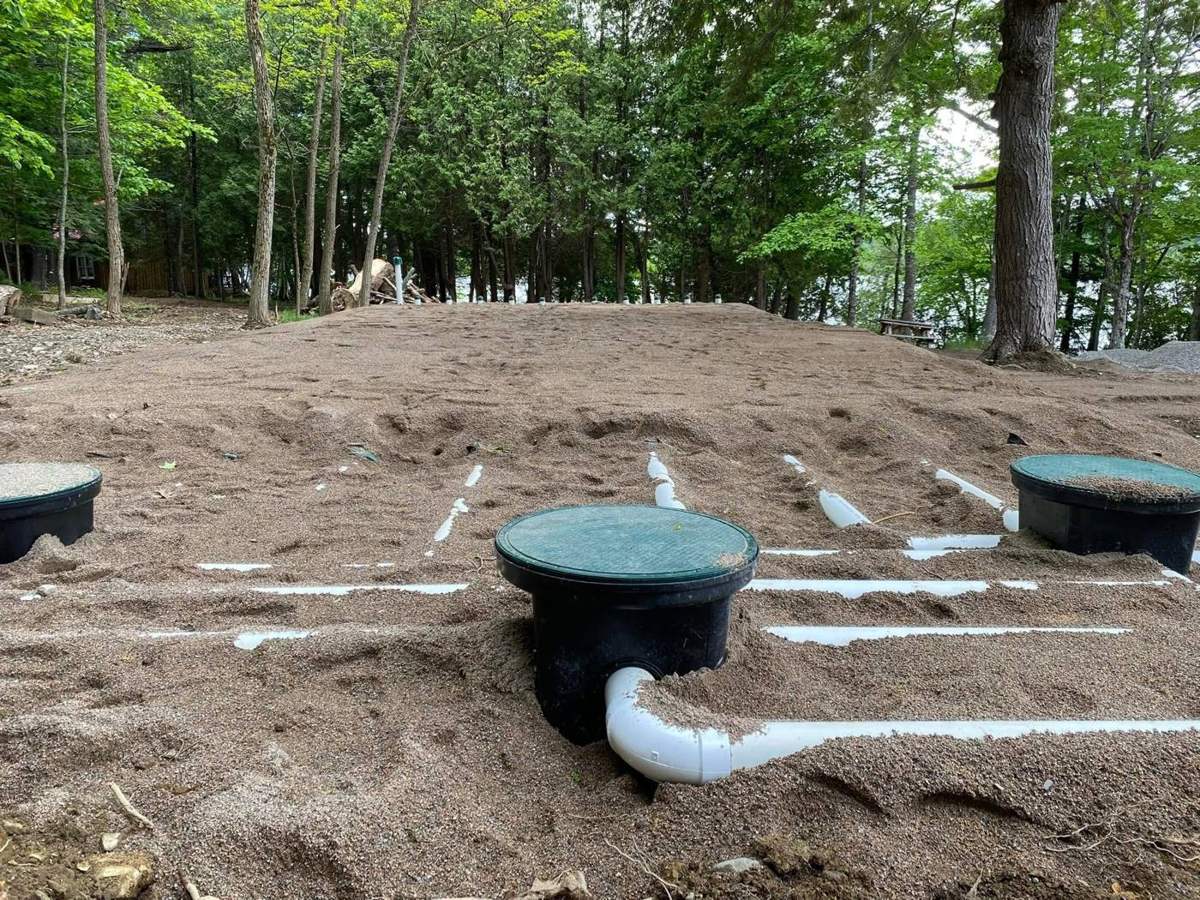 New septic field with green distribution box lids and white lateral pipes in sand